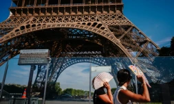 Des touristes se protègent du soleil avec des éventails en passant devant la tour Eiffel, fermée plus tôt en raison de la canicule, le 11 juillet 2026 à Paris