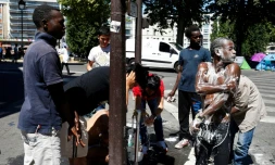 Les habitants d'un campement de migrants installé sous le métro aérien font leur toilette, le 19 juillet 2016 dans le nord-est de Paris