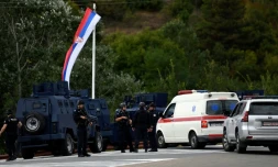 Des policiers kosovars montent la garde sous un drapeau serbe à l'entrée du village de Banjska, dans le nord du Kosovo, le 24 septembre 2023