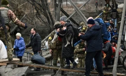 Une femme porte un chien en traversant un pont détruit à Irpin (Ukraine) pendant des bombardements, le 5 mars 2022