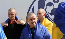 Photo diffusée par le Quartier général de coordination pour le traitement des prisonniers de guerre, le 19 août 2026, montrant d'anciens prisonniers de guerre ukrainiens, enveloppés dans des drapeaux nationaux, près d'un bus après un échange effectué dans un lieu tenu secret