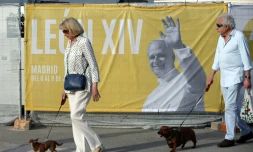 Deux personnes promènent leur chien près d'une affiche annonçant la venue du pape Léon XIV, le 5 juin 2026 à Madrid