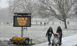 Des promeneurs passent prĂšs d'un panneau appelant Ă se faire tester au Covid-19, dans un parc de Londres sous la neige, le 24 janvier 2021