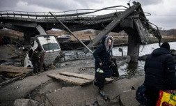 Des personnes fuient la ville d'Irpin, au nord-ouest de Kiev en traversant une riviÚre prÚs d'un pont détruit, le 13 mars 2022