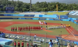 Les équipes japonaises et australiennes de softball écoutent les hymnes nationaux avant le début du premier match de la compétition olympique, marquant le début officiel des épreuves des JO de Tokyo, le 21 juillet 2021 à Fukushima, à deux jours de la cérémonie d'ouverture