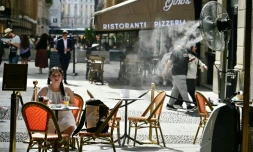 Une jeune fille assise à la terrasse d'un marchand de glaces, sur laquelle un ventilateur-brumisateur a été installé pour se protéger de la chaleur à Milan en Italie, le 27 mai 2026