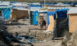 Un homme assis au milieu de cabanes de fortune dans la "Jungle" de Calais, le 16 mars 2016