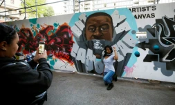 Une femme, genou à terre et poing levé, devant une peinture murale représentant George Floyd, le 11 juin 2020 à Graffiti Alley, à Toronto