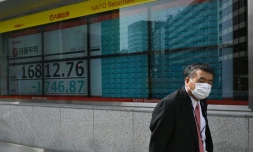 Un homme masqué passe devant un écran de la Bourse de Tokyo en chute, le 13 mars 2020