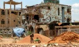Un ouvrier pellette des cailloux dans une brouette près d'un bâtiment fortement endommagé de la banlieue de Lambab, à la périphérie de Khartoum, le 30 juillet 2025 au Soudan