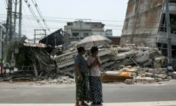 Des personnes se tiennent à côté d'un bâtiment endommagé à Mandalay, en Birmanie, le 30 mars 2025