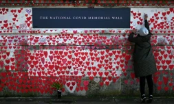 Une femme écrit sur le mur commémoratif national dédié aux victimes du Covid, le 3 mars 2024 à Londres