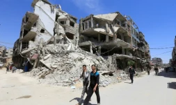 Des Syriens passent devant des immeubles détruits, le 16 avril 2018 à Douma, lors d'une visite organisée par l'armée syrienne dans la Ghouta orientale