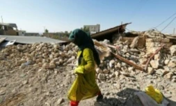 Photo prise le 15 novembre 2017 à Kouik (nord-ouest de l'Iran) montrant une femme marchant dans les décombres d'un bâtiment détruit par le séisme du 12 novembre 