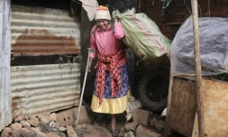Molly Aluoch s'appuie sur une béquille pour porter un sac de déchets plastiques usagés collectés dans le bidonville de Kibera, à Nairobi, le 11 août 2025 au Kenya