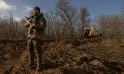 Un soldat ukrainien surveille le ciel en cas d'attaque de drones pendant qu'une tractopelle creuse des tranchées dans la région de Zaporijjia, le 30 janvier 2024