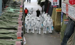 Des employés en combinaison de protection pulvérisent du désinfectant dans les allées d'un marché de la ville de Daegu, le 23 février 2020 en Corée du Sud
