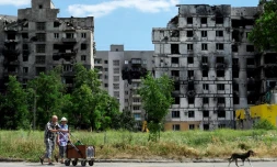 Un couple transporte des bouteilles d'eau devant un bùtiment détruits à Marioupol, Ukraine le 1er juillet 2022