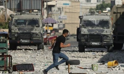 Un Palestinien court devant des véhicules militaires israéliens stationnés dans la vieille ville de Naplouse en Cisjordanie occupée, le 9 août 2022     