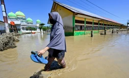 Une habitante marche près d'une mosquée dans zone inondée, le 30 novembre 2025 à Meureudu en Indonésie