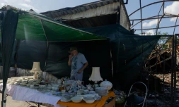 Vadym vend des objets sur son étal du marché aux puces de Potchaïna endommagé par une frappe russe, le 9 août 2026 à Kiev, en Ukraine
