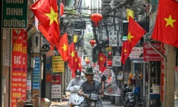 Un homme porte un ventilateur le long d'une rue bordée de drapeaux nationaux vietnamiens à Hanoï, le 30 avril 2024