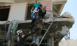 Des bénévoles du service de défense civil syrien évacuent des gens d'un immeuble détruit par des bombardements, dans un quartier rebelle d'Alep le 23 avril 2016