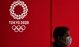 Une femme avec un masque passe devant le logo des JO de Tokyo de 2020 le 24 mars 2020 dans la capitale nippone.