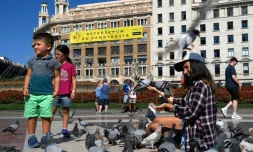 Sur cette photo prise le 13 septembre 2017 sur la place de Catalogne à Barcelone, une femme et des enfants nourrissent des pigeons devant une banderole "Oui. Le référendum c'est la démocratie" appelant à voter au référendum prévu le 1er octobre