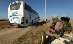 Des membres du groupe jihadiste Hayat Tahrir al-Cham regardent passer un bus en direction de Foua et Kefraya, deux villages de la province d'Idleb, d'où seront évacuées des milliers de personnes, le 18 juillet 2018 en Syrie