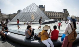 Touristes se rafraßchissant à la fontaine face à la pyramide du Louvre, à Paris le 7 août 2018