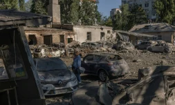 Une femme se tient près de voitures détruites et de bâtiments endommagés après une frappe russe à Kiev, le 20 août 2026