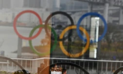Les anneaux olympiques se réflétant sur une vitrine dans le parc de bord de mer d'Odaiba (baie de Tokyo) et un Japonais se protégeant du nouveau coronavirus avec un masque, le 8 mars 2020