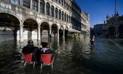 Un couple assis sur des chaises de café observe la place Saint-Marc inondée, à Venise le 14 novembre 2019
