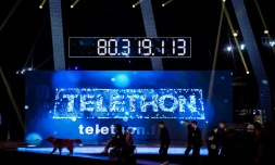 Des invités marchent devant le compteur de dons de l'édition 2016 du Téléthon, à Paris, le 4 décembre