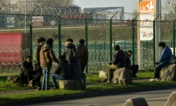 Des migrants derrière un grillage barbelé d'un parking pour camions près de la N216 conduisant au terminal de ferry, le 12 janvier 2018 à Calais 
