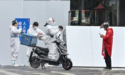 Un livreur (d) prÚs d'employés en combinaison de protection devant un quartier confiné de Shanghai aprÚs l'apparition de nouveaux cas de Covid-19, le 17 mars 2022 en Chine