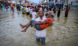 Un homme porte une personne âgée dans une rue inondée, le 30 novembre 2025 à Wellampitiya au Sri Lanka