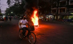 Un couple à vélo passe devant un feu allumé par les manifestants anti-junte à Rangoun, le 3 avril 2021