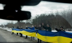 Des personnes tiennent un drapeau ukrainien le long d'une route pour accueillir un convoi de soldats libérés par les Russes après un échange de prisonniers, le 6 mars 2026 dans un lieu non précisé dans le nord de l'Ukraine