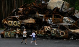 Des enfants jouent devant des carcasses de voitures calcinées, dont certaines ont été peintes par des artistes locaux, à Irpin le 9 août 2022
