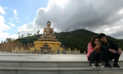 Un couple assis regarde l'écran d'un téléphone portable à cÎté d'une statue de Bouddha à Thimphou, la capitale du Bouthan, le 25 août 2018