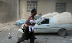 Un homme avec un bébé s'enfuit aprÚs des bombardements sur Kafr Batna, dans la banlieue de Damas, le 30 septembre 2016