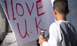 Un jeune migrant réalise une pancarte, "j'aime le Royaume-Uni", à Calais le 31 octobre 2016