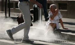 Une touriste assise à côté de la vapeur d'eau sortant d'une bouche d'aération dans le quartier de Wall Street, à New York, alors qu'une alerte à la chaleur extrême a été émise, le 23 juin 2025