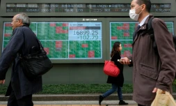 Des piétons passent devant un tableau d'indices boursiers, le 17 mars 2020 à Tokyo, au Japon