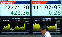 Un passant marche devant des écrans montrant le prix d'actions et le taux de change de devises face au dollar américain à Tokyo, au Japon, le 15 octobre 2018