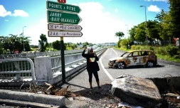 Une manifestante portant un t-shirt aux couleurs de l'UGTG (Union générale des travailleurs de Guadeloupe) lève le poing devant du matériel brûlé aux Abymes, près de Pointe-à-Pitre en Guadeloupe, le 24 novembre 2021