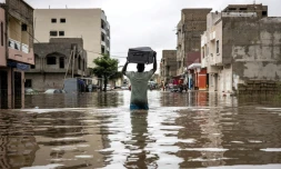 Un homme porte une valise sur sa tête en traversant une rue inondée de Dakar, au Sénégal, le 20 août 2021