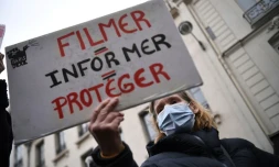 Une manifestante tient une pancarte "filmer = informer = protéger" durant une manifestation contre la loi sécurité globale devant le Sénat le 16 mars 2021
